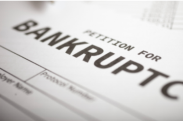Close-up of hands reviewing and preparing bankruptcy petition paperwork on a desk with legal documents and a laptop.